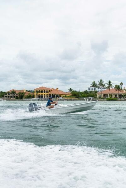 2025 BlueZones Boatworks 16' Flats cruising on water near luxury waterfront homes.