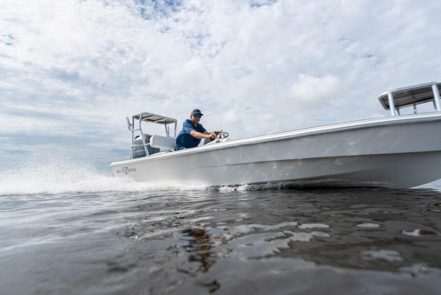 2025 BlueZones Boatworks 16' Flats boat speeding on water under cloudy sky.