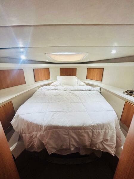 Cozy bedroom interior of 1988 Bertram 54' yacht with white bedding and wooden accents.
