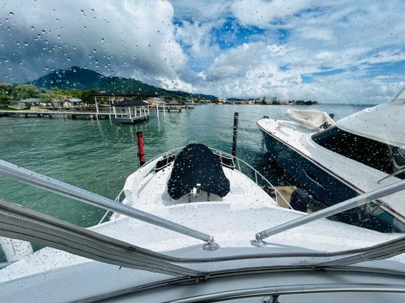 1988 Bertram 54' yacht docked in scenic marina, viewed through rain-speckled window.