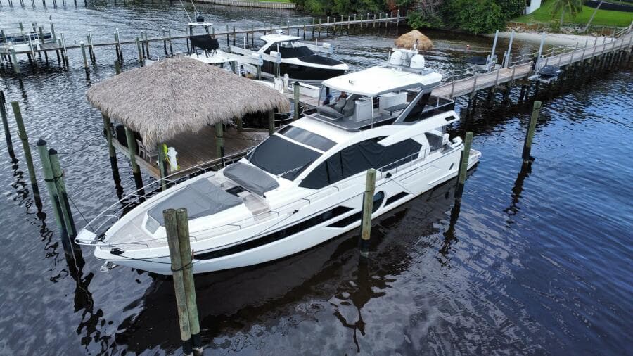 2024 Aicon 66 Vivere yacht docked at a marina with thatched roof hut.