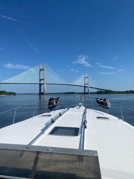 1993 Sea Ray 440 Sundancer cruising towards a suspension bridge under clear blue skies.