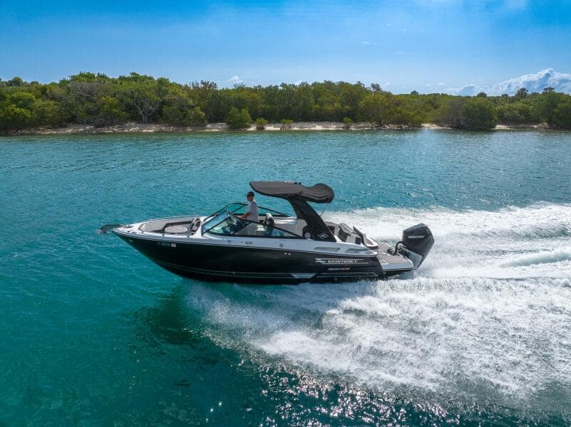2023 Monterey 255 Super Sport boat cruising on clear blue water near a lush shoreline.