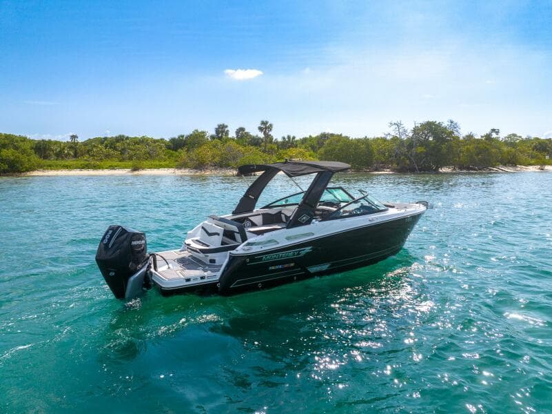 2023 Monterey 255 Super Sport boat on clear blue water near a lush green shoreline.
