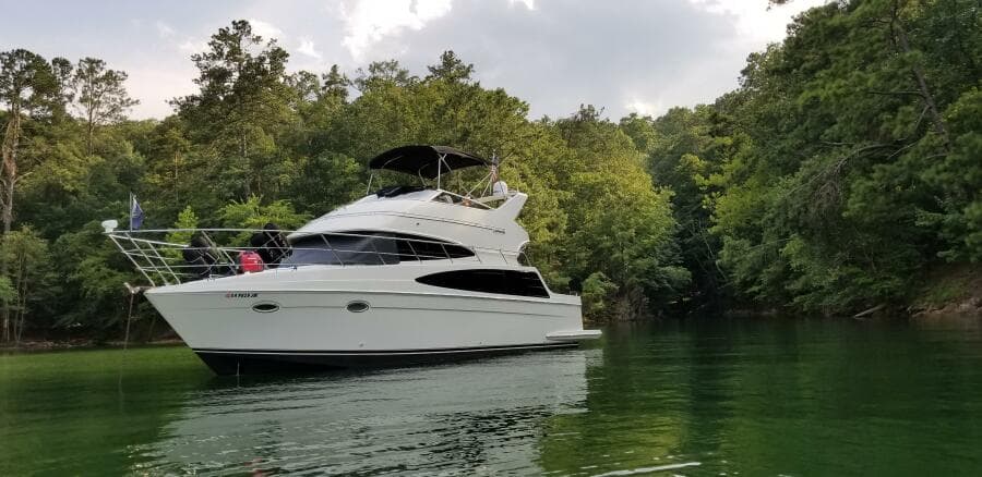 2004 Carver 360 Sport Sedan yacht on a serene lake surrounded by lush trees.