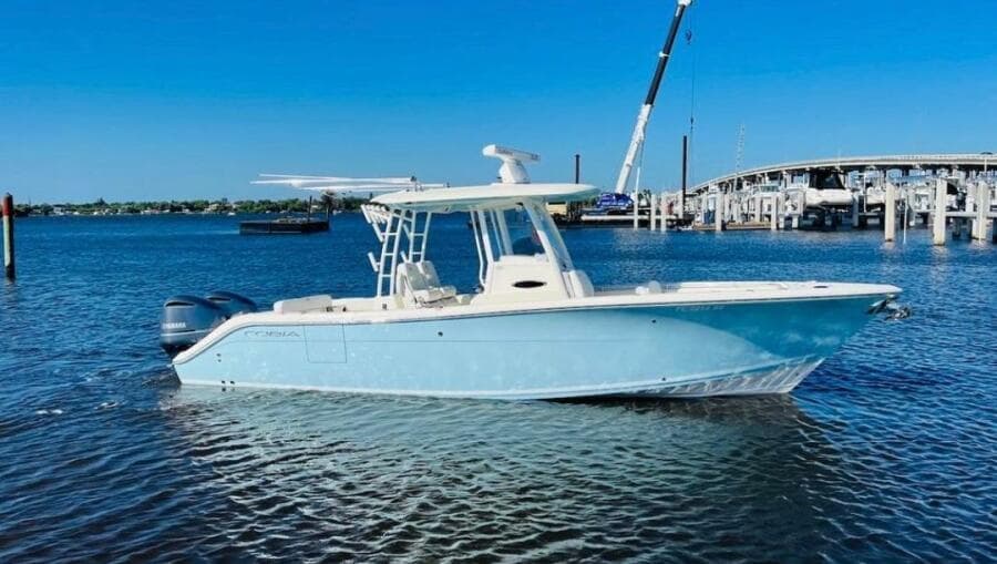 2021 Cobia 301 Center Console boat on water, clear sky, marina background.